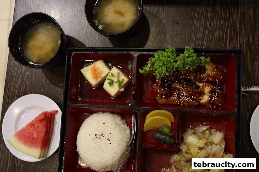 A bento box meal with grilled eel, rice, tofu, pickles, and soup.