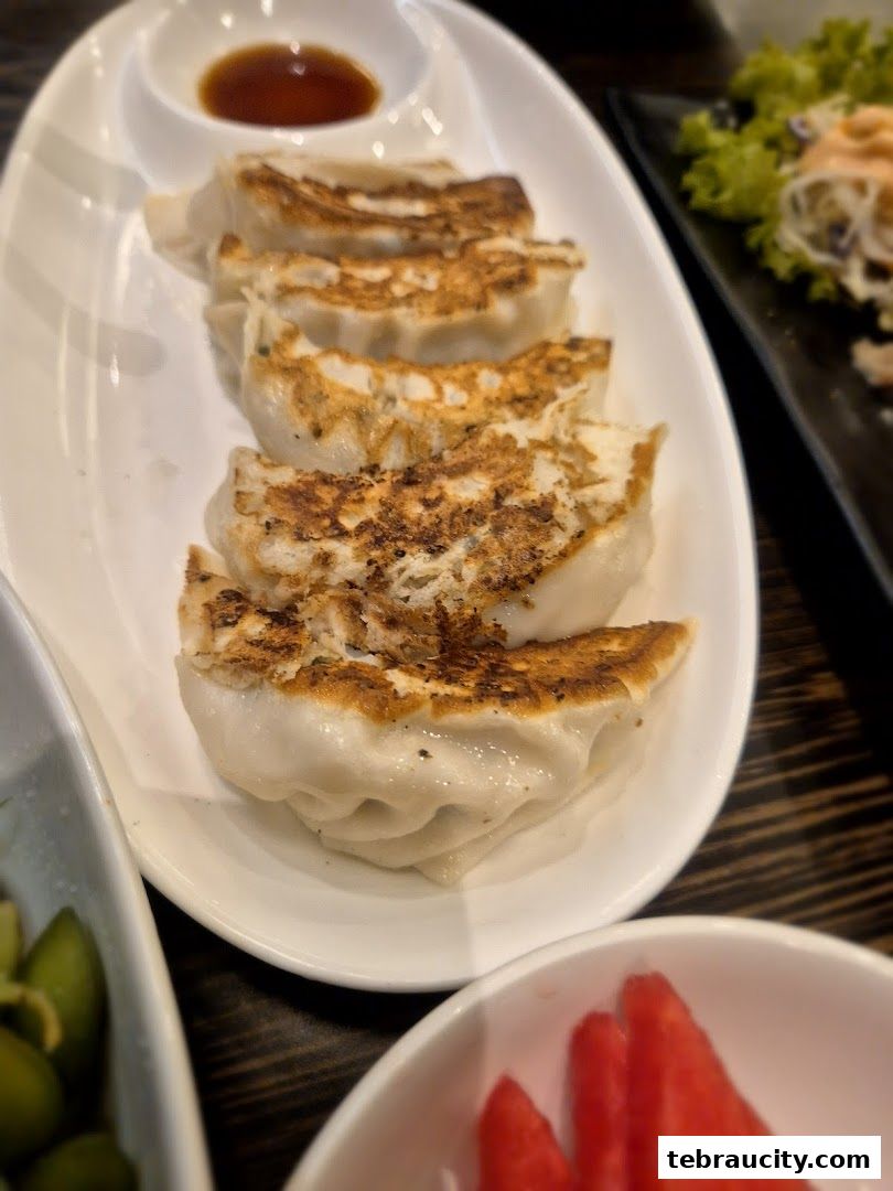 A plate of pan-fried gyoza with a side of dipping sauce.