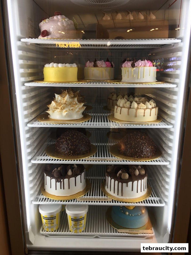 A display refrigerator filled with various beautifully decorated cakes and ice cream tubs.