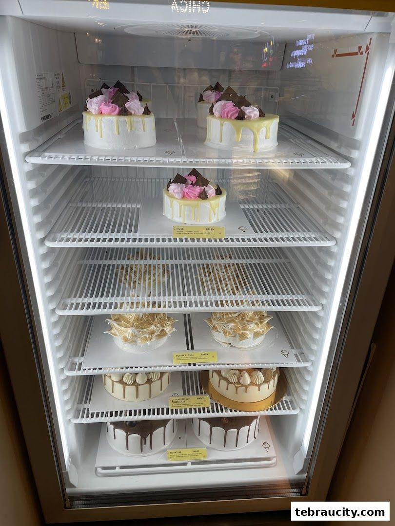 A refrigerator display case filled with beautifully decorated cakes of various flavors and designs.