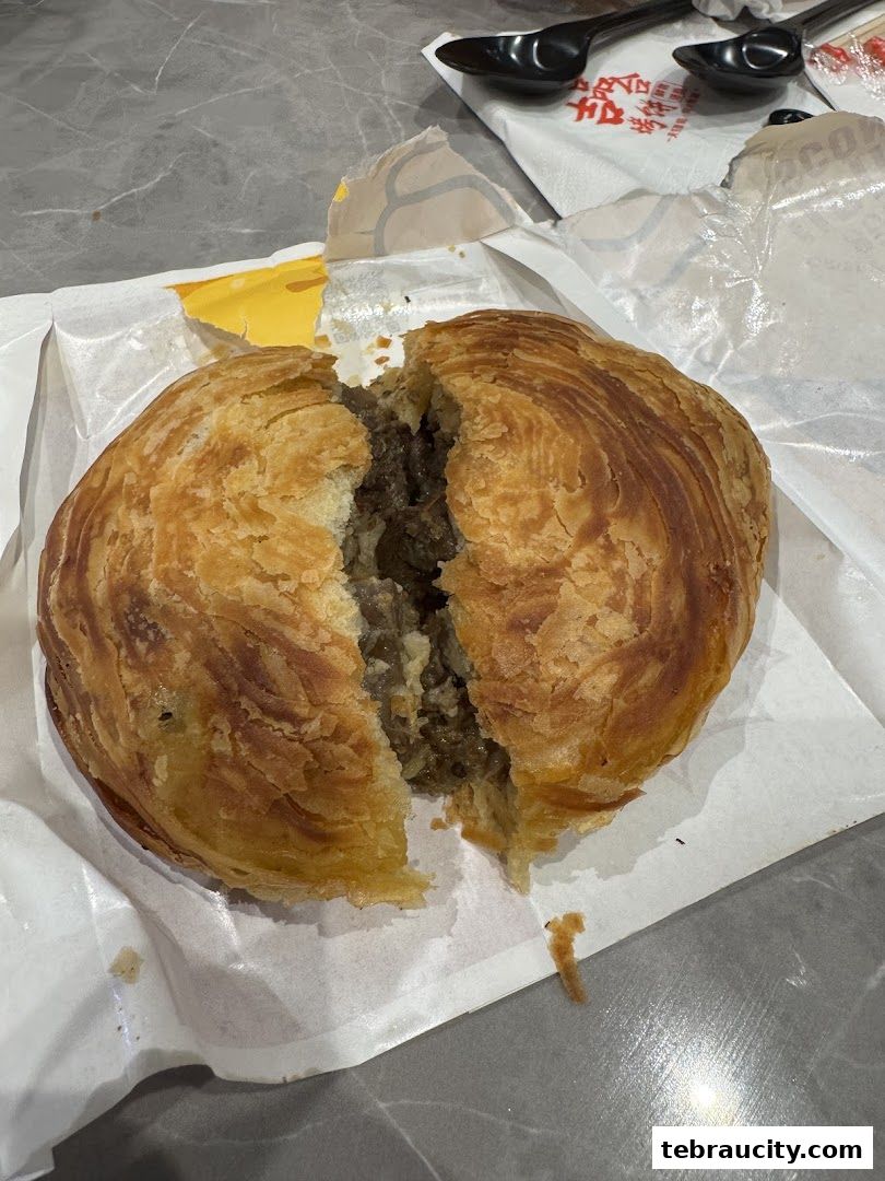 A golden-brown, flaky scone filled with savory meat filling, split in half.