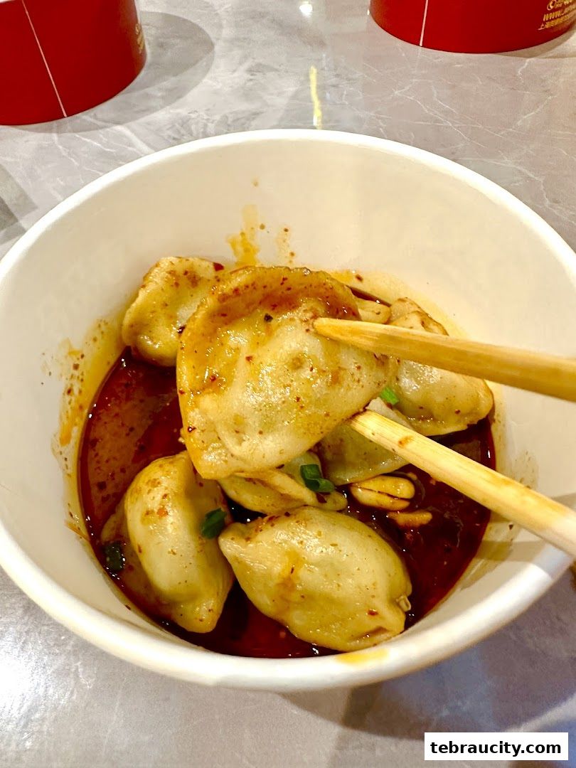 A close-up shot of delicious dumplings in a spicy chili oil sauce, being picked up with chopsticks.