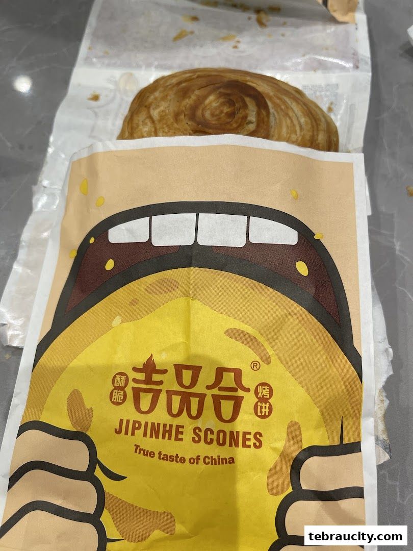 A golden-brown scone peeking out of a brightly colored paper bag with a cartoon mouth.