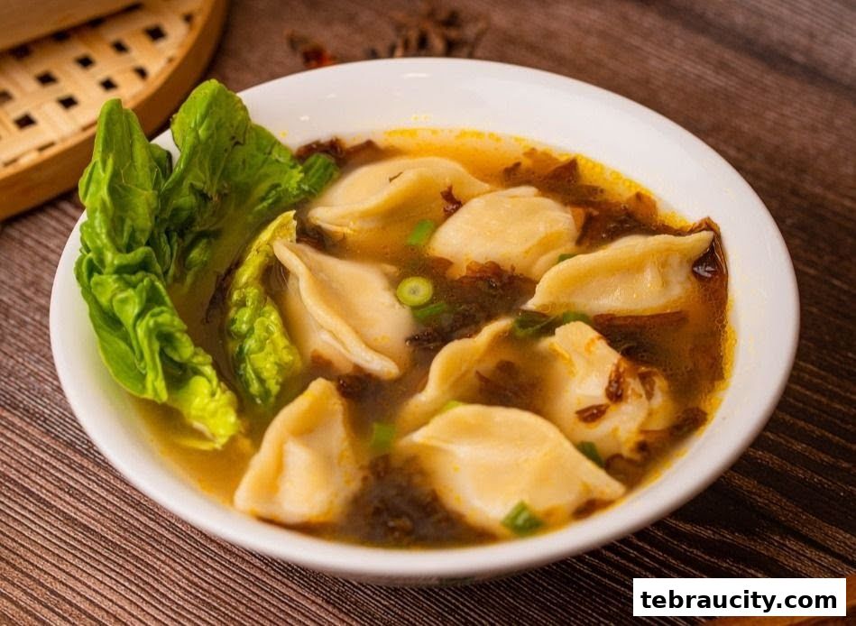 A bowl of delicious dumplings in broth with lettuce and green onions.