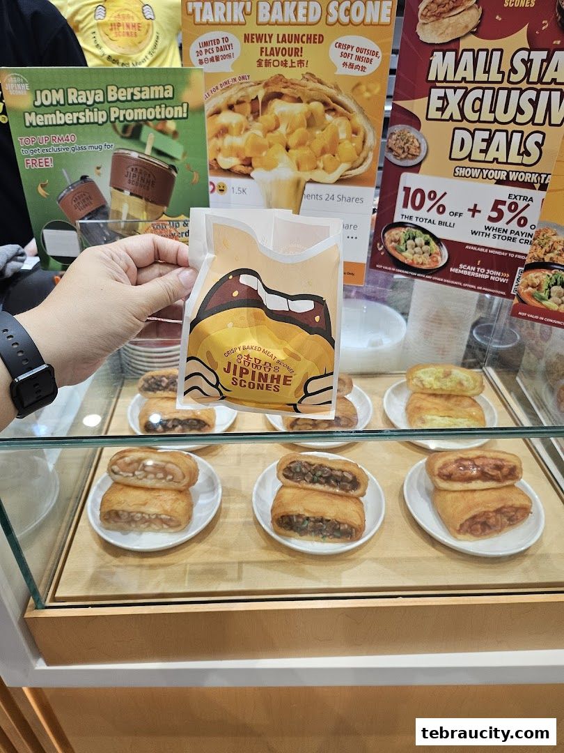 A hand holds a Jipinhe Scones bag in front of a display of baked goods.