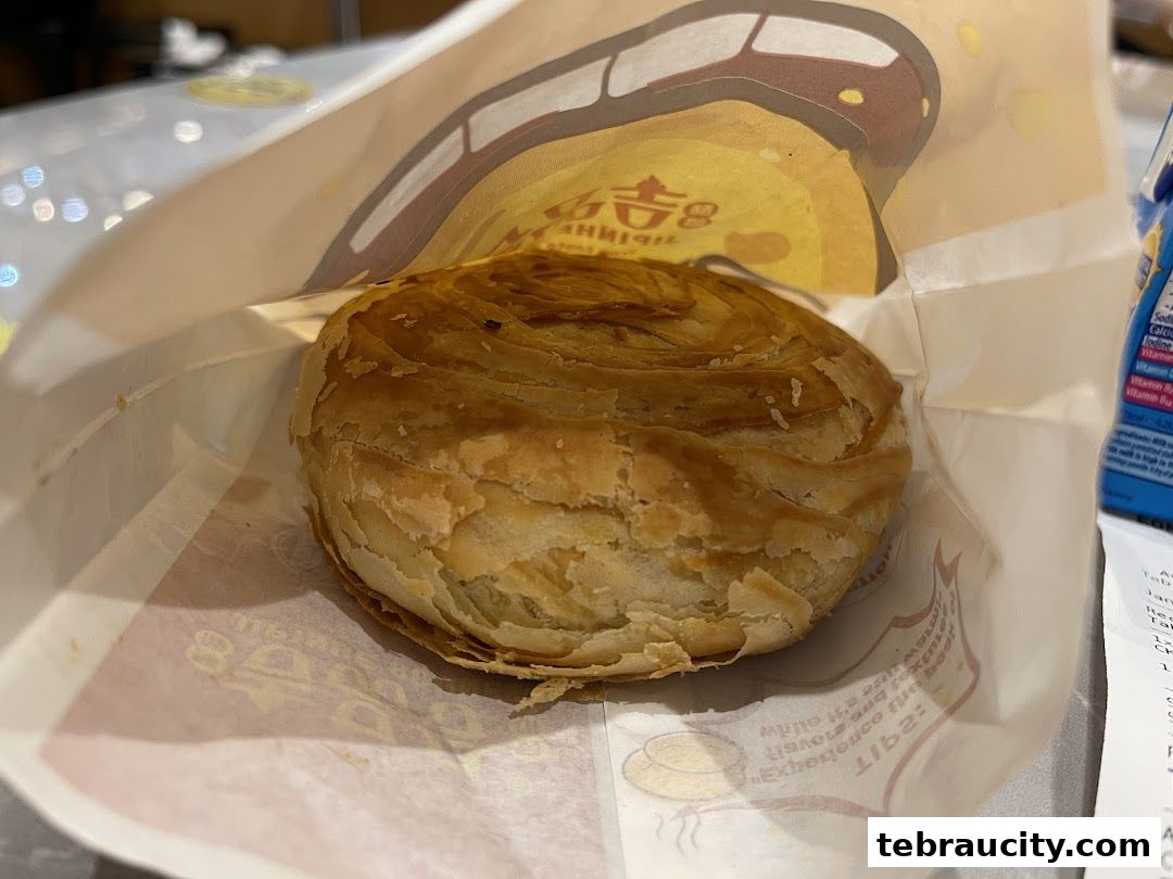 A golden-brown, flaky scone is presented in a branded paper bag.