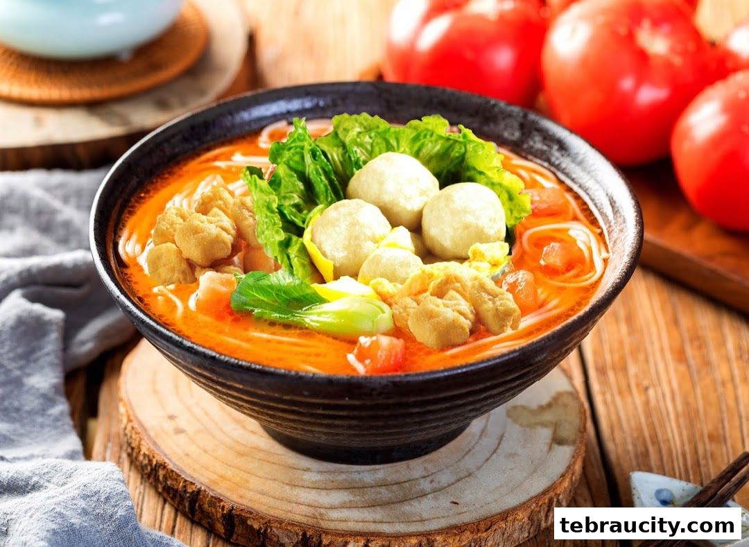 A close-up of a steaming bowl of noodles with meatballs, vegetables, and crispy toppings.