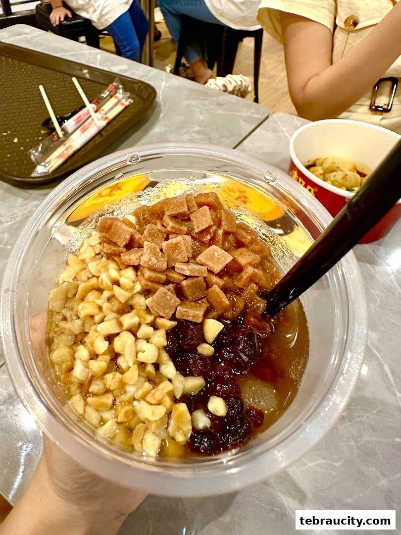 A close-up of a dessert cup with peanuts, red beans, and brown sugar cubes.