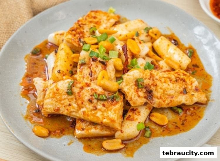 A plate of savory fried tofu with peanuts and scallions in a spicy sauce.