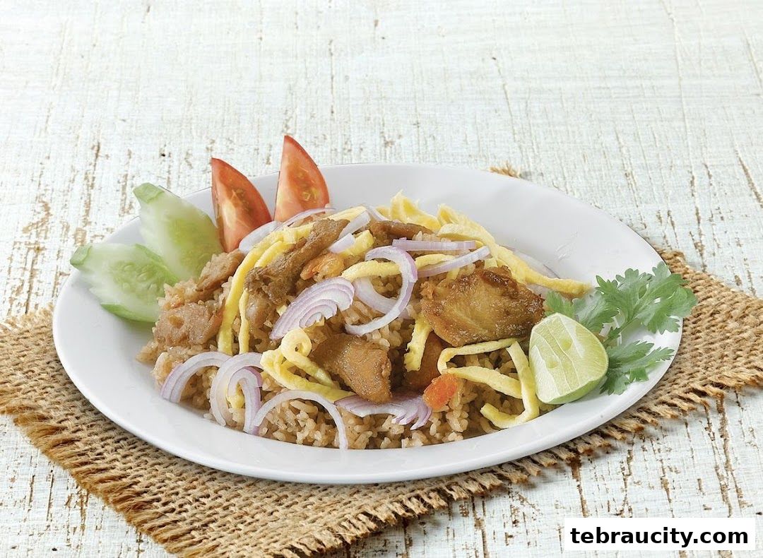 A plate of fried rice with meat, egg, onions, cucumber, tomato, and lime.