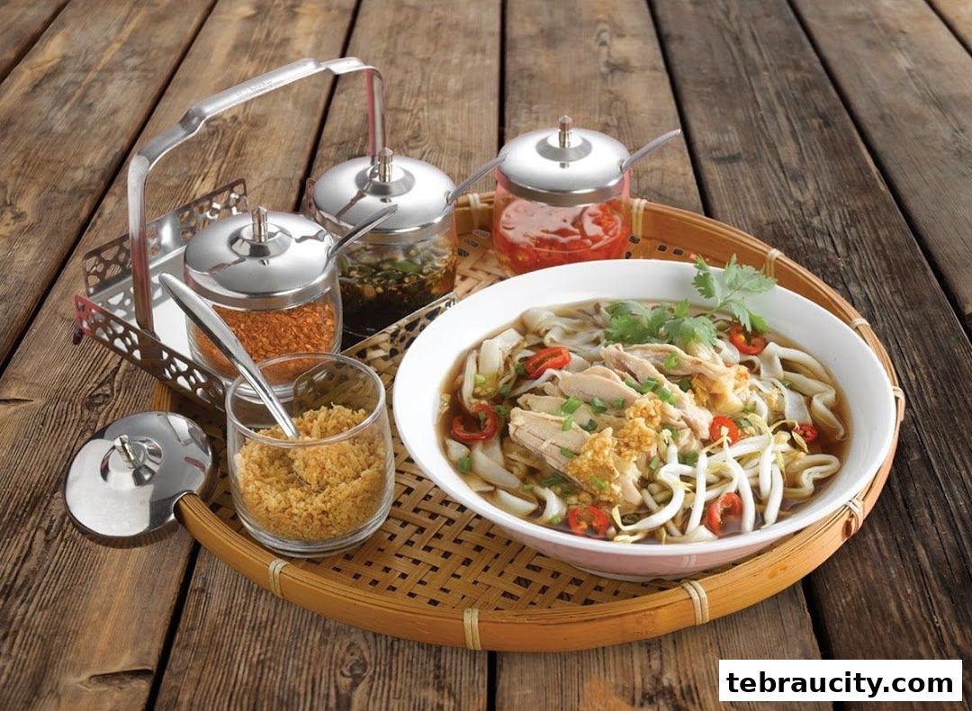 A bowl of noodle soup with chicken, bean sprouts, chili, and herbs, served with condiments.