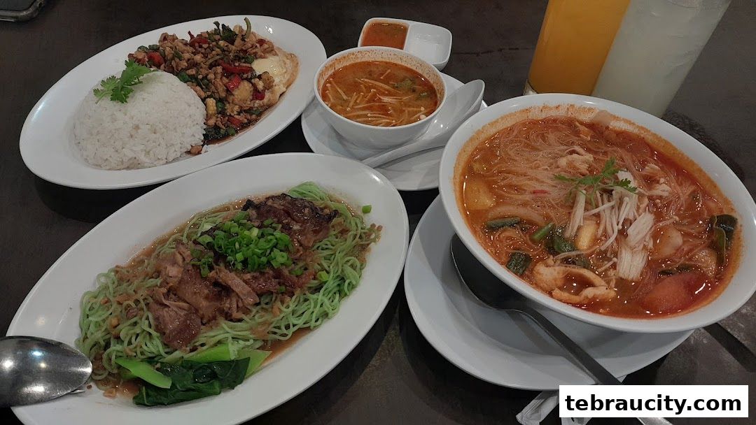 A spread of delicious Thai dishes including Tom Yum soup, green noodles with meat, and basil chicken with rice.