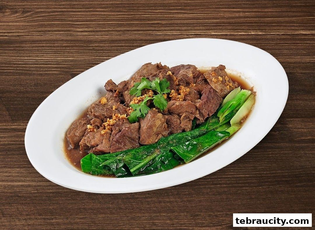 A plate of tender braised beef with garlic and green vegetables on a wooden table.