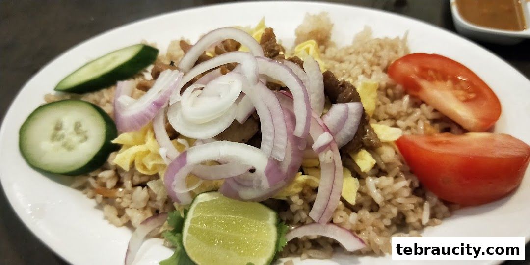 A plate of fried rice with sliced onions, tomatoes, cucumber, and lime.