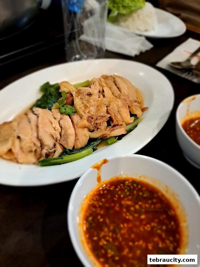 A plate of sliced chicken with greens and a side of dipping sauce.
