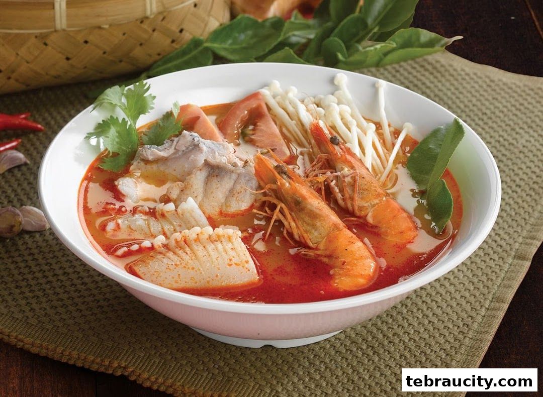 A steaming bowl of Tom Yum soup with prawns, fish, and enoki mushrooms.