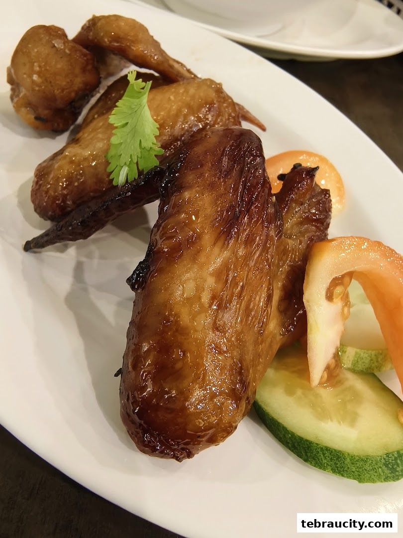 A plate of delicious, glazed chicken wings served with fresh cucumber and tomato slices.