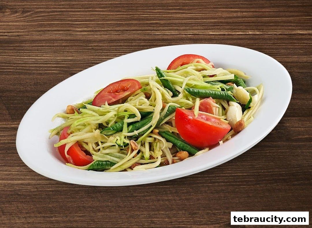A white oval plate filled with a fresh green papaya salad with tomatoes and peanuts.