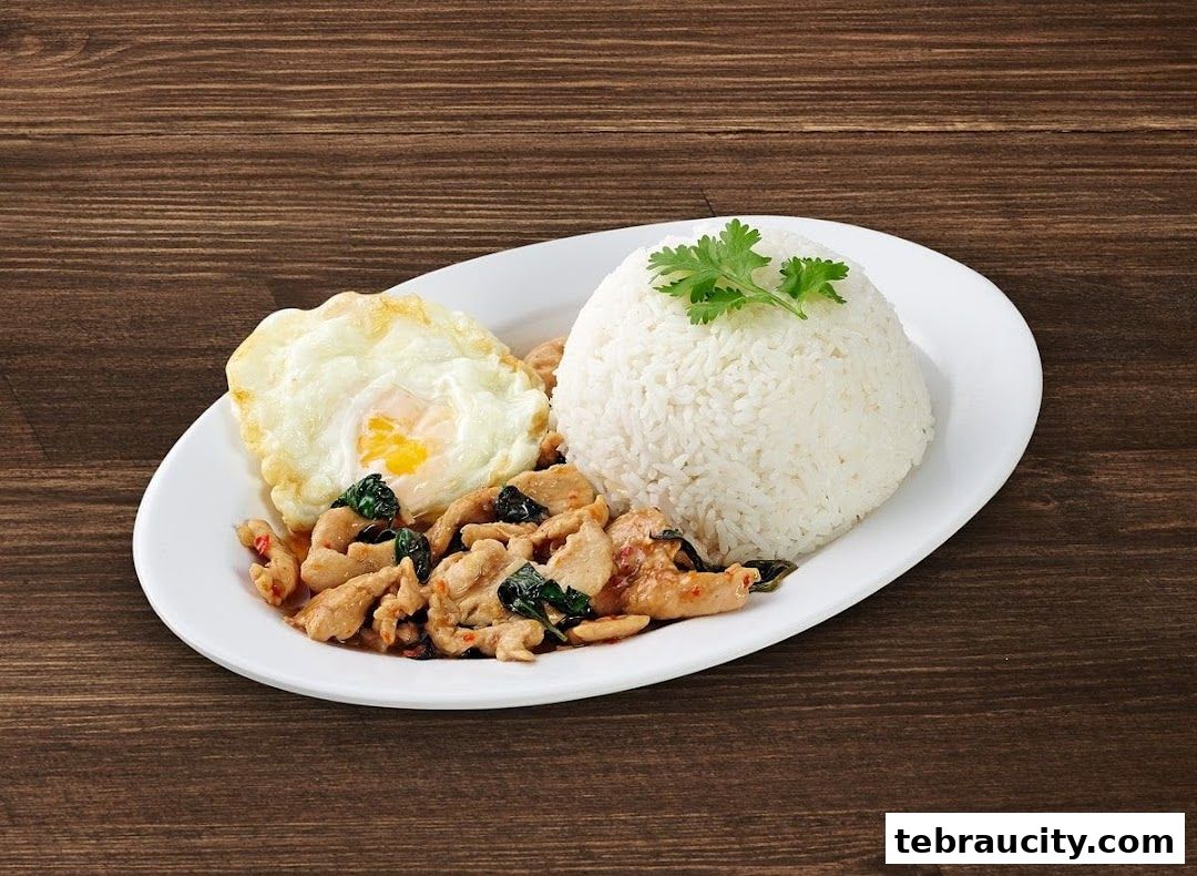 A plate of Thai basil chicken with a fried egg and rice on a wooden table.