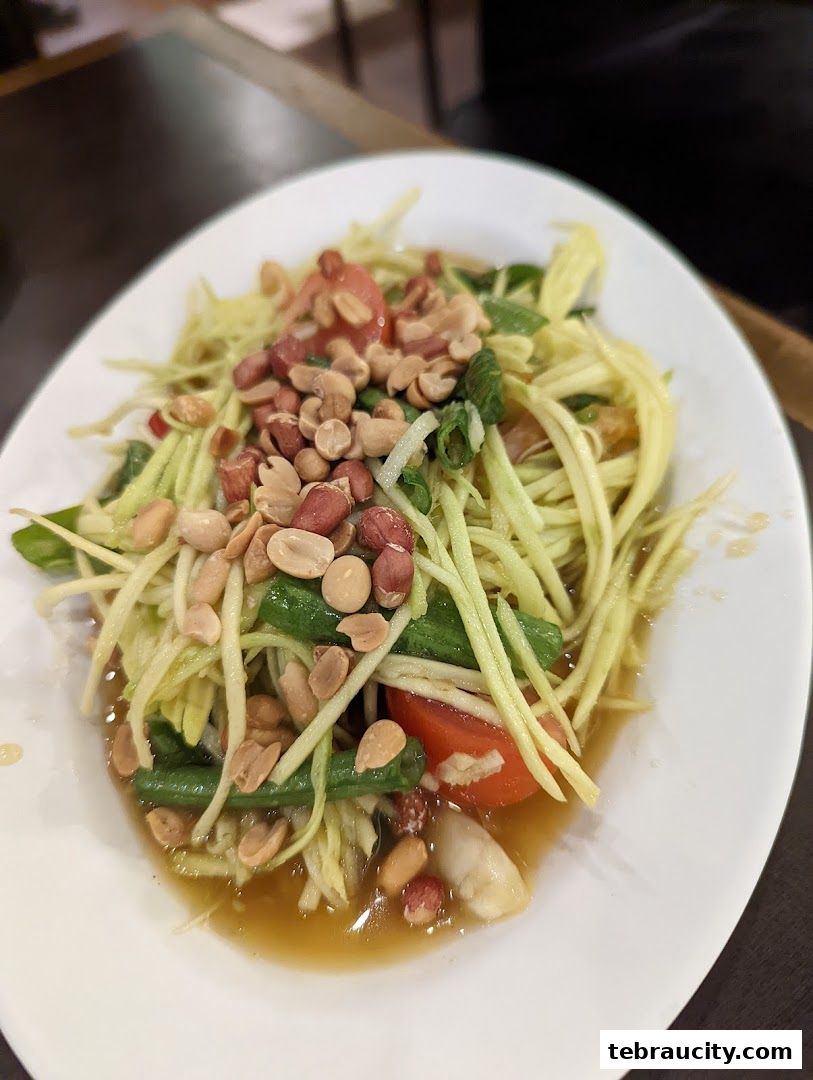A plate of green papaya salad with peanuts and tomatoes.