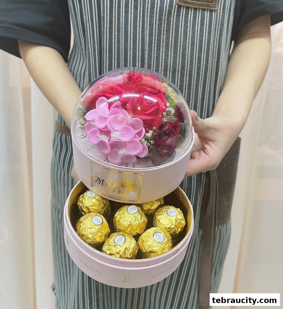 A person holds two pink boxes, one with flowers and the other with Ferrero Rocher chocolates.
