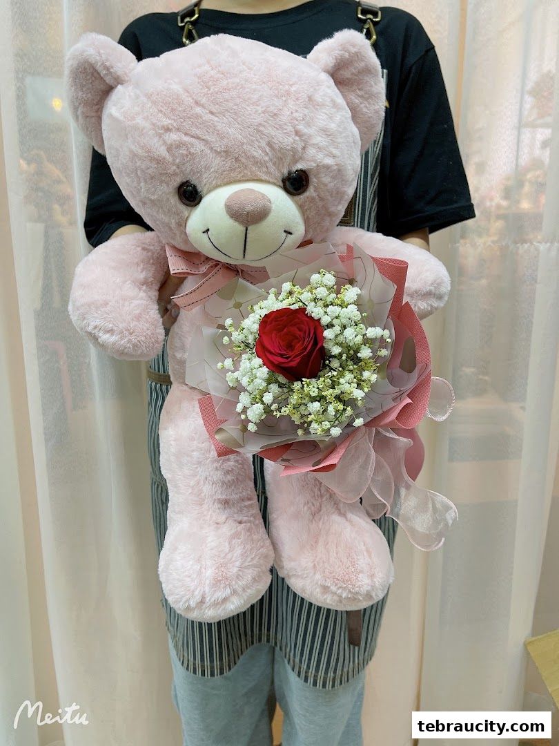 A person holds a large pink teddy bear with a bouquet of flowers.