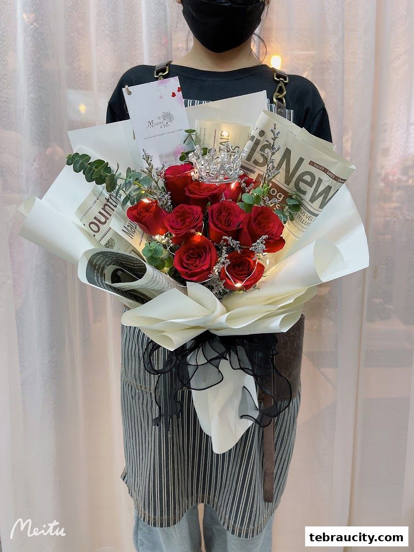 A person holds a bouquet of red roses adorned with a crown and fairy lights.