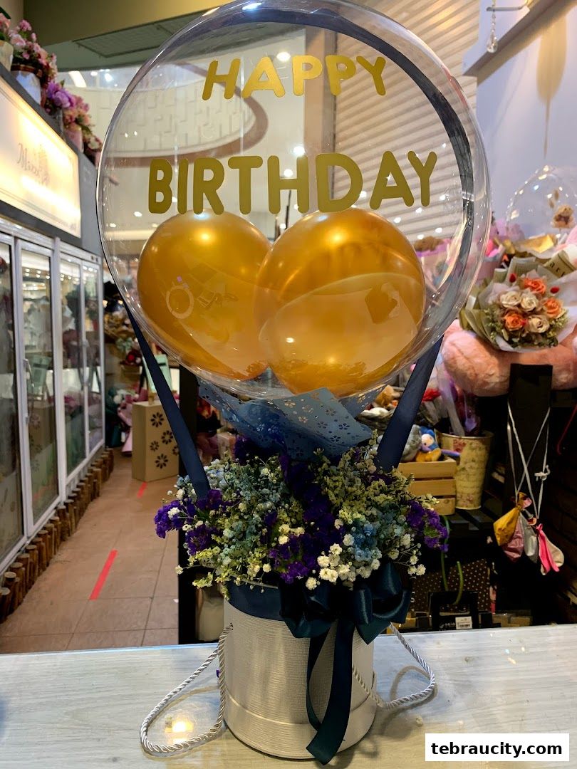 A floral arrangement in a box with a clear balloon featuring 'Happy Birthday' text.