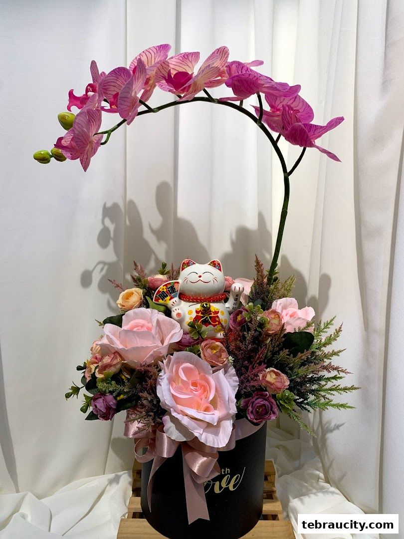 A floral arrangement featuring pink orchids, roses, and a Maneki-neko cat.