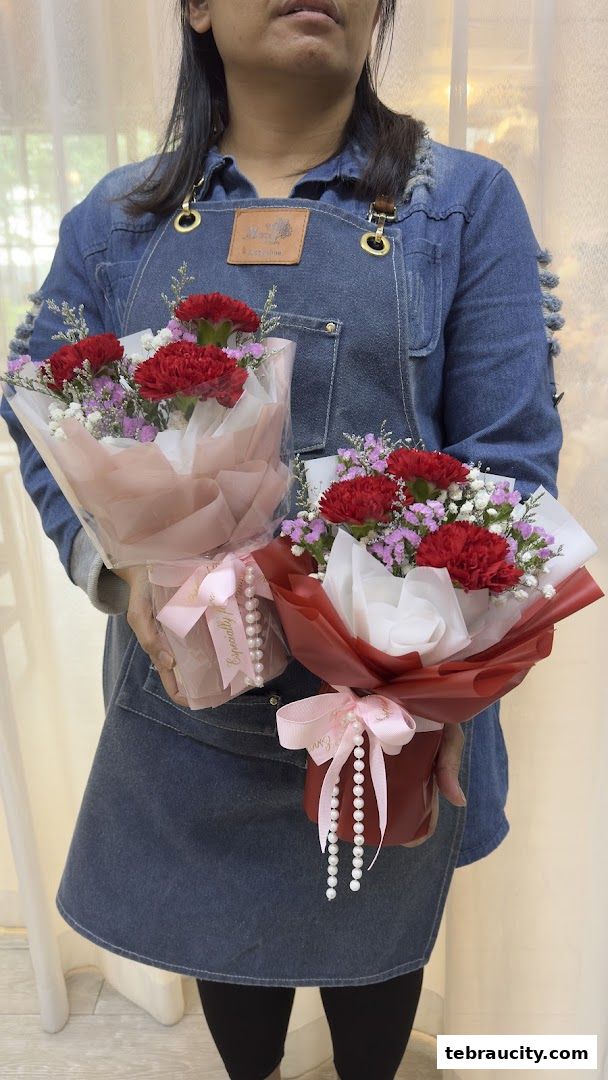 A person in a denim apron holds two bouquets of red carnations and baby's breath.