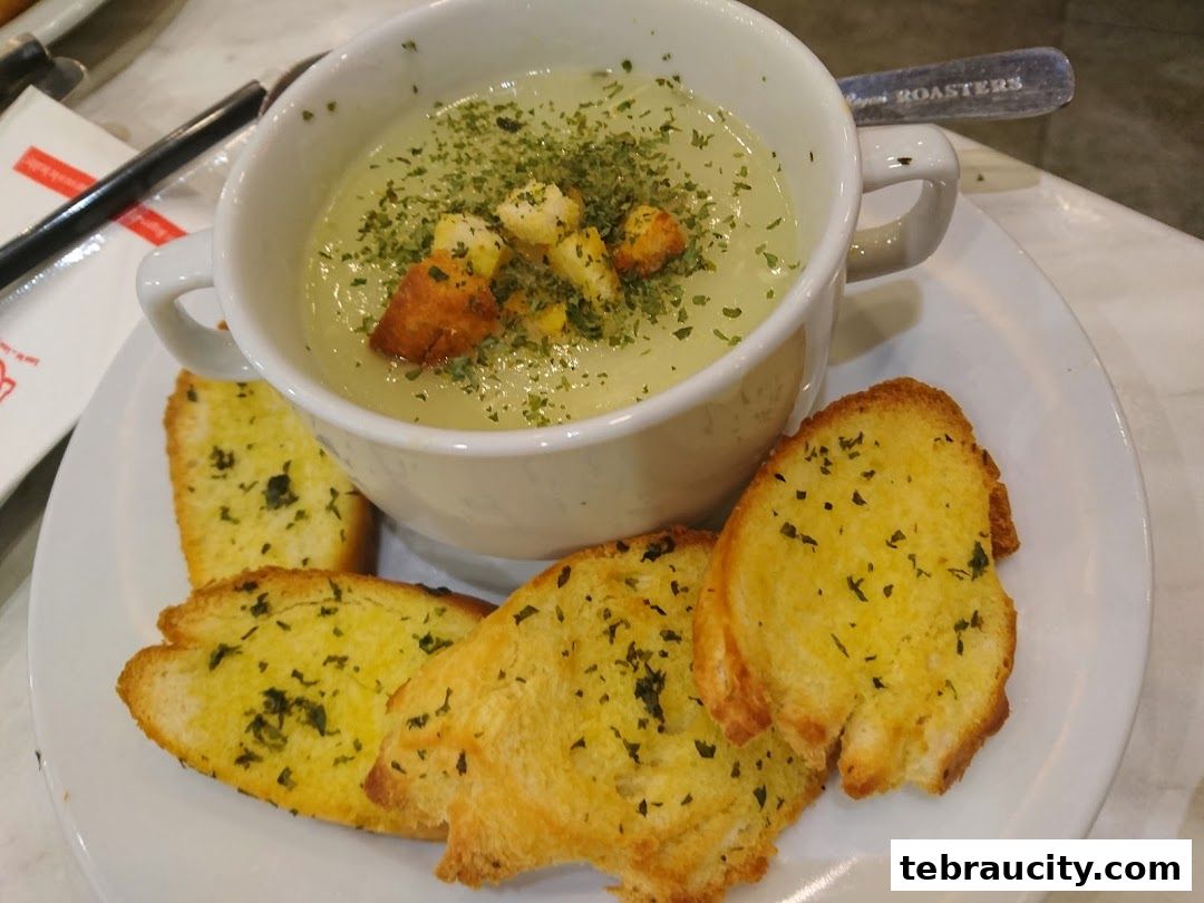 A bowl of creamy soup topped with croutons and herbs, served with garlic bread.