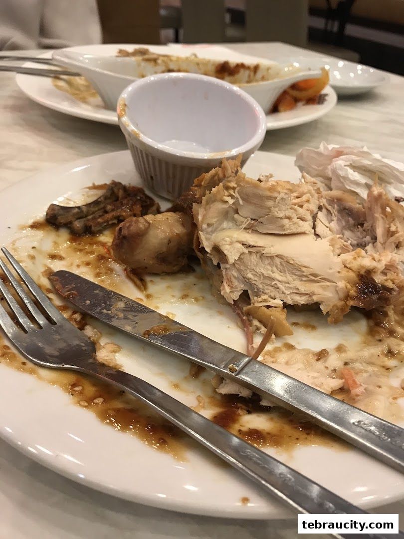 A close-up of a partially eaten roasted chicken on a plate with cutlery.