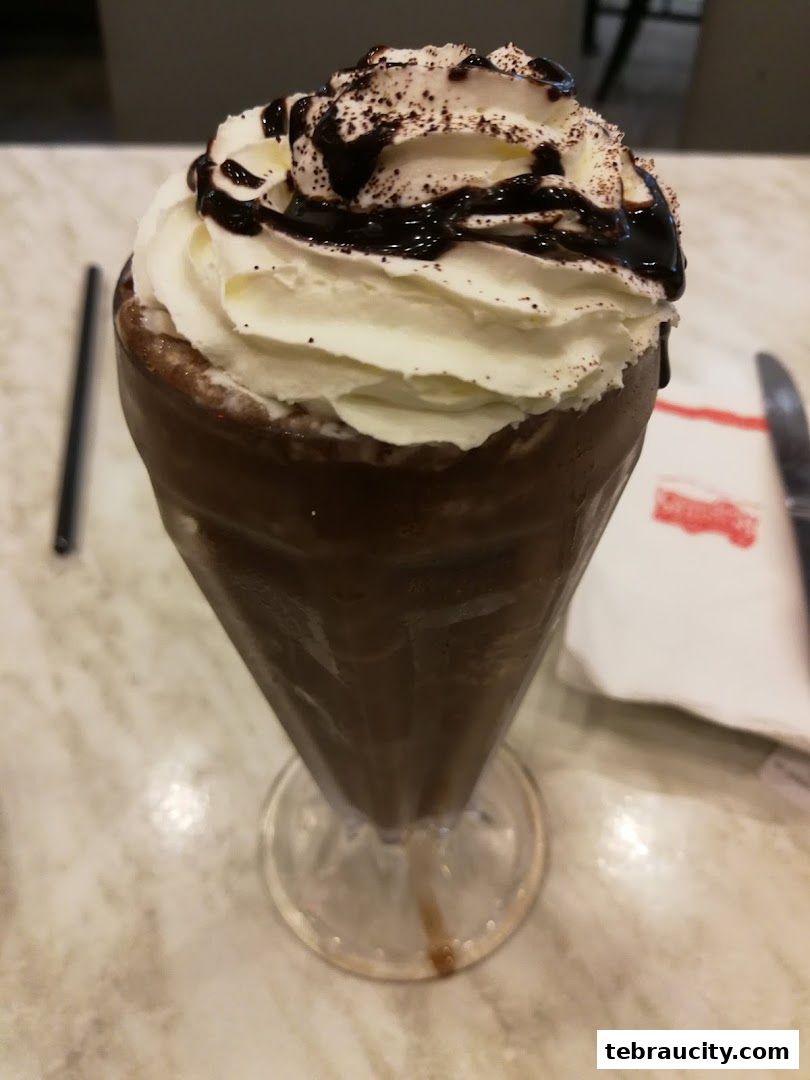 A tall glass of chocolate milkshake topped with whipped cream and chocolate syrup.