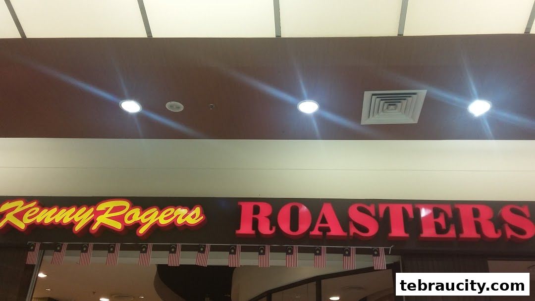The Kenny Rogers Roasters sign is illuminated with red and yellow lettering, adorned with Malaysian flags.