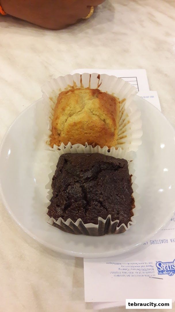 Two freshly baked muffins, one banana and one chocolate, served on a white plate.