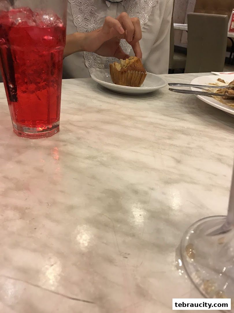 A person is about to eat a muffin with a red drink on a marble table.