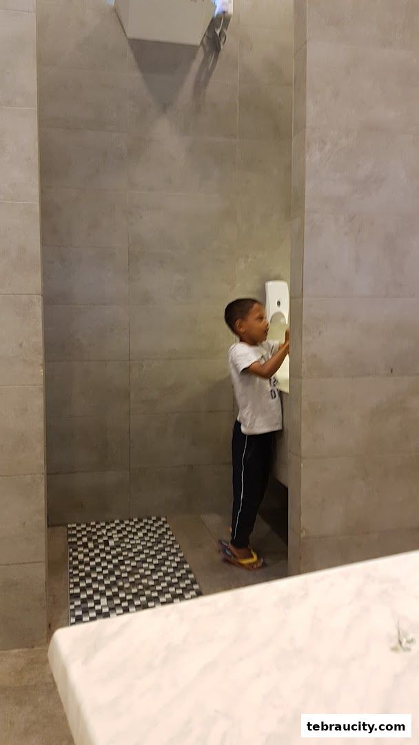 A young boy washes his hands in a modern restroom with tiled walls.