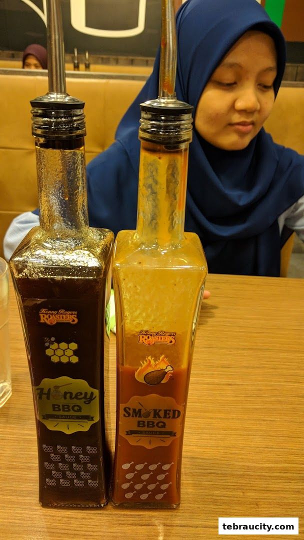 Two bottles of Kenny Rogers Roasters BBQ sauce, Honey BBQ and Smoked BBQ, on a table.