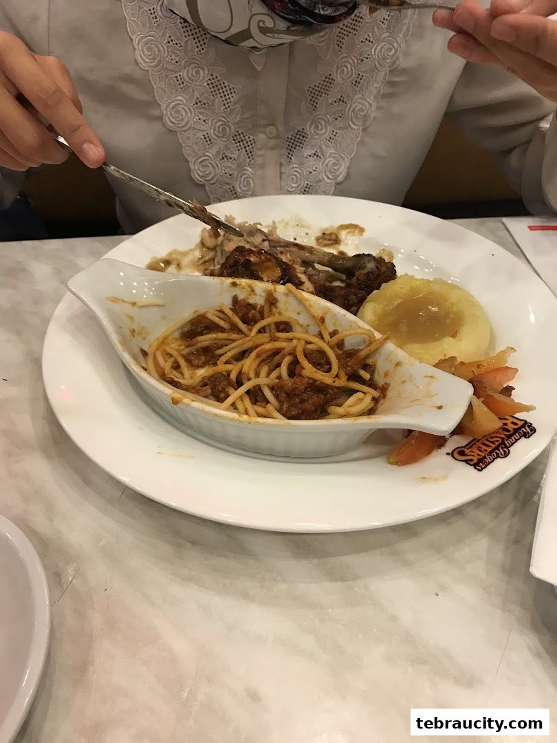 A person is eating a meal with spaghetti, mashed potatoes, and chicken.