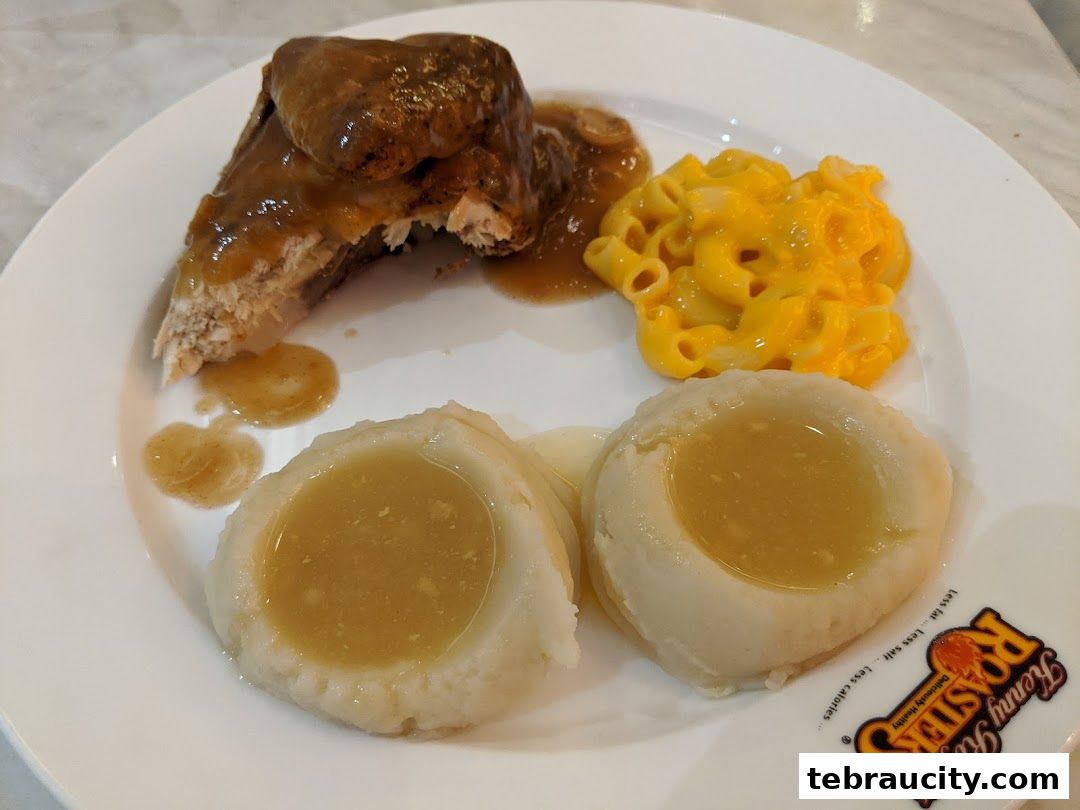 A plate of roasted chicken with mashed potatoes, macaroni and cheese, and gravy.