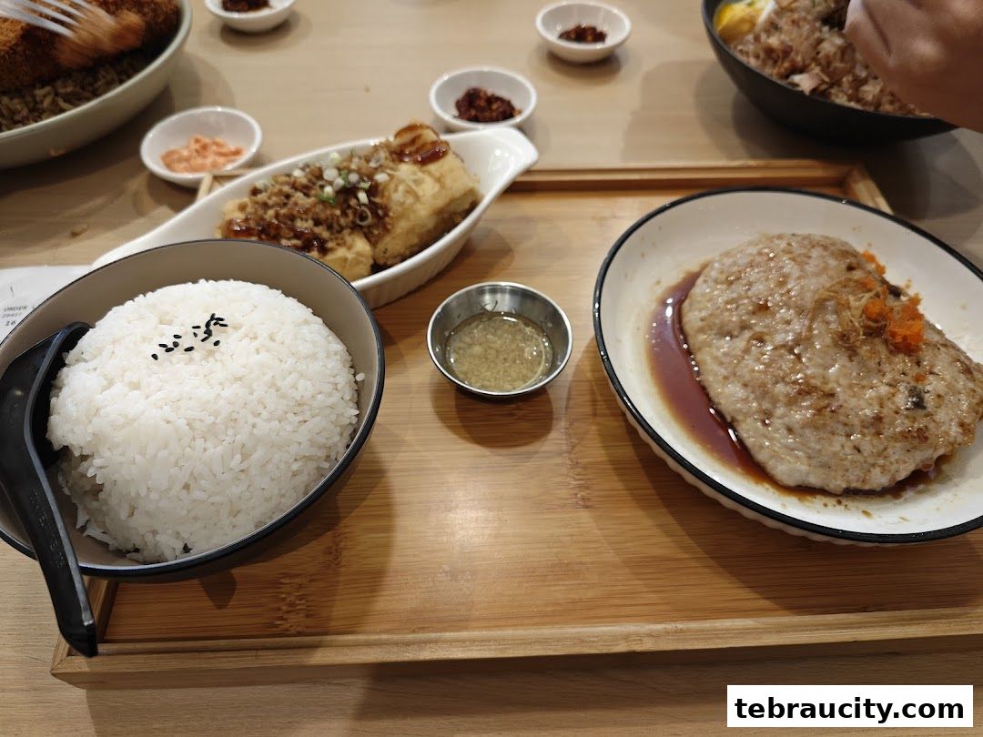 A close-up of a delicious meal featuring rice, fried tofu, and a patty served on a wooden tray.