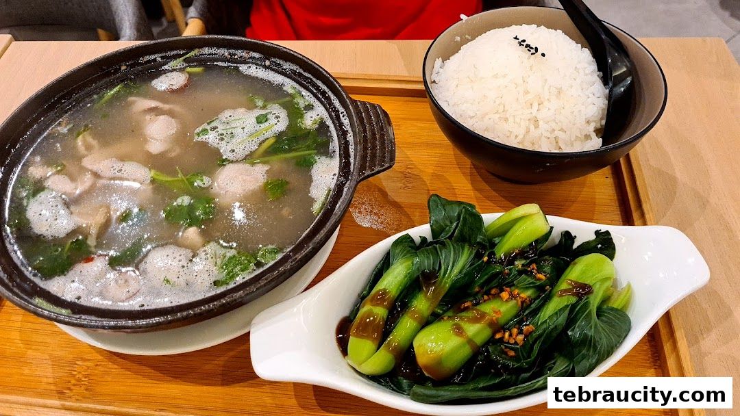 A steaming bowl of soup with meat and greens, served with rice and a side of stir-fried vegetables.
