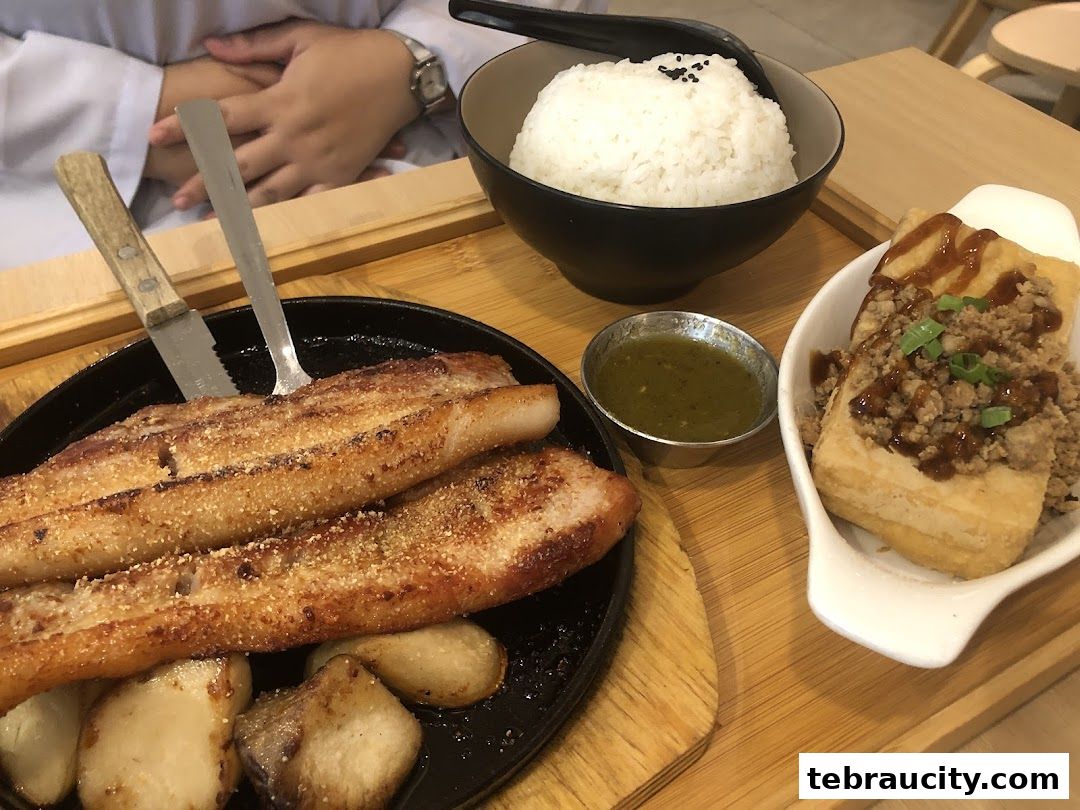 A close-up of a delicious meal featuring grilled pork belly, rice, fried tofu, and dipping sauce.