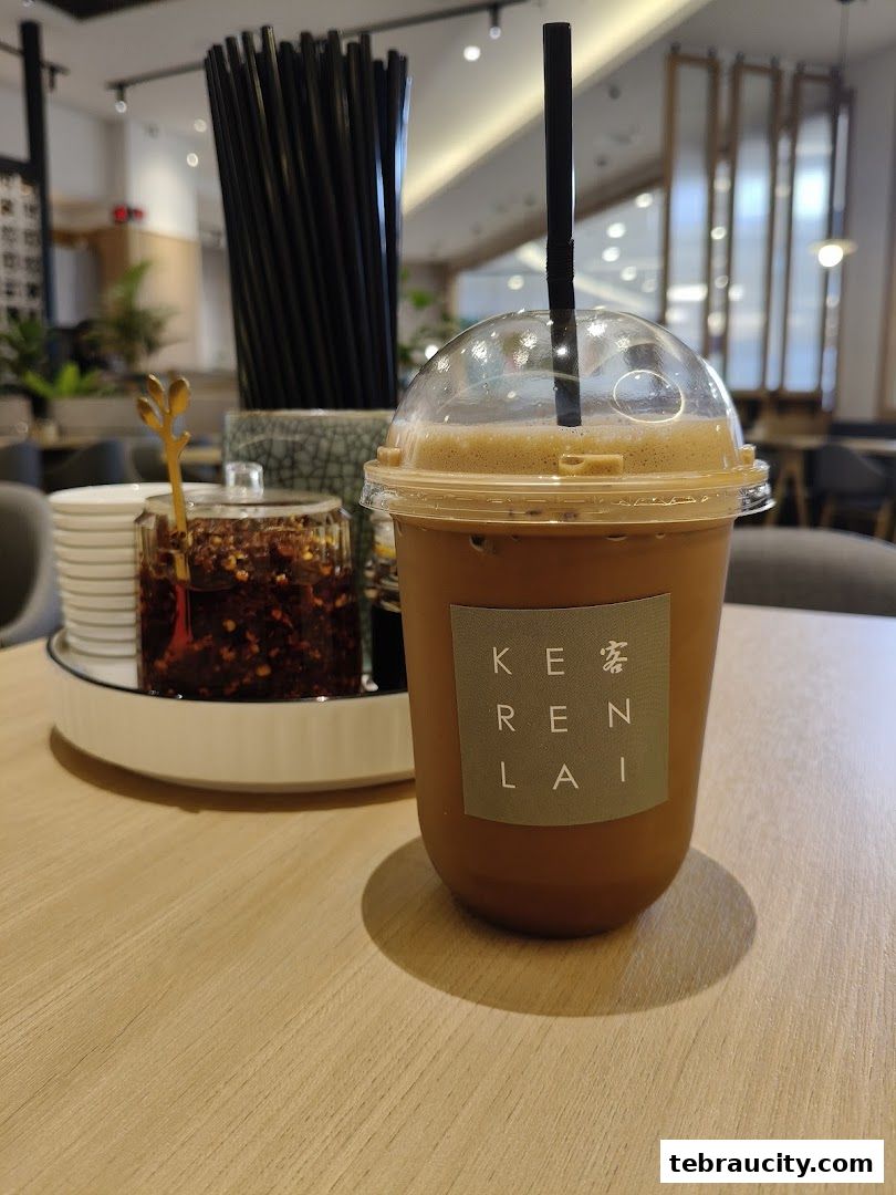 A refreshing iced beverage with a straw sits on a wooden table next to a condiment dish.