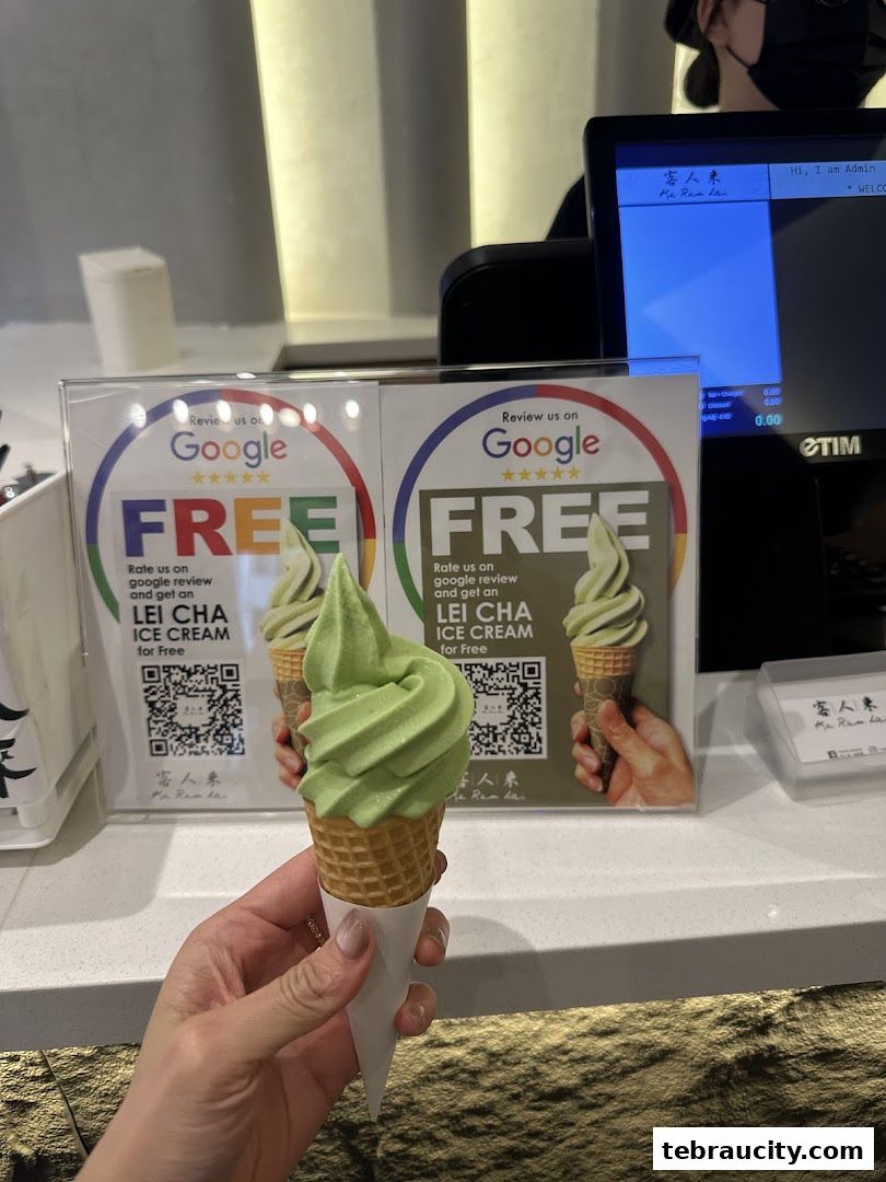 A hand holds a green soft-serve ice cream cone in front of a promotional display.
