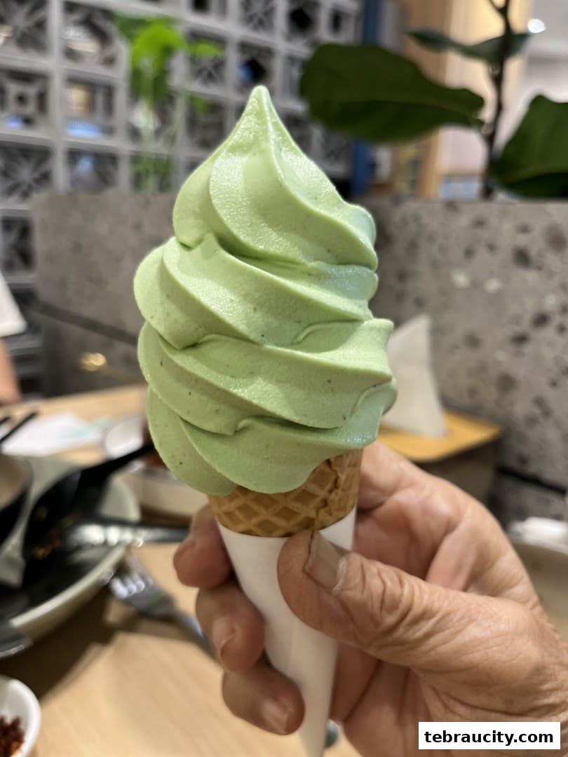 A hand holds a green soft-serve ice cream cone in a waffle cone.