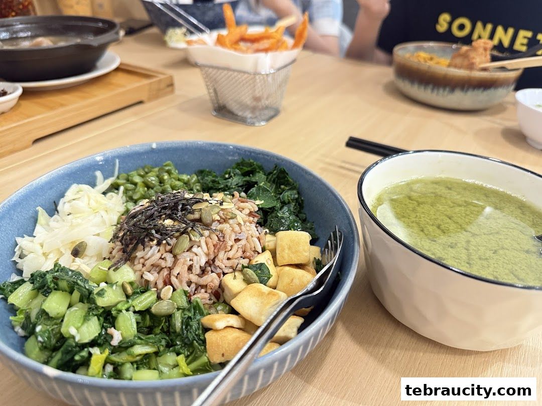 A close-up of a healthy grain bowl with various vegetables and a side of soup.