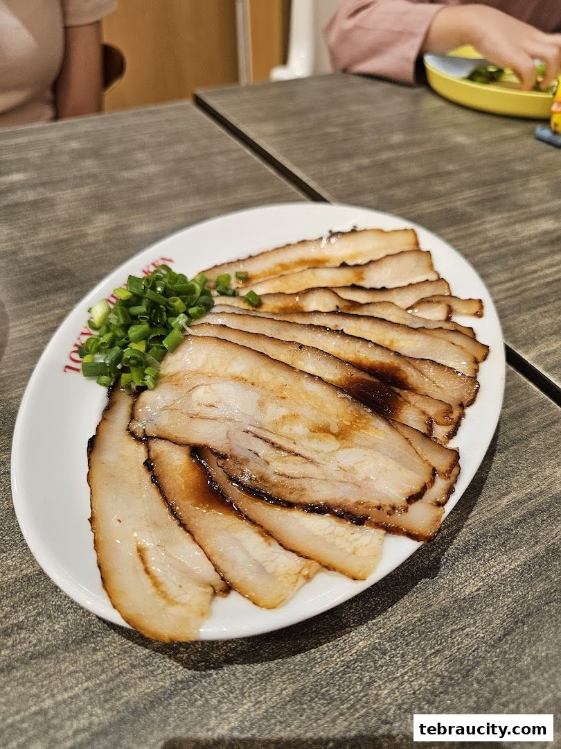 A plate of sliced chashu pork with green onions and sauce.