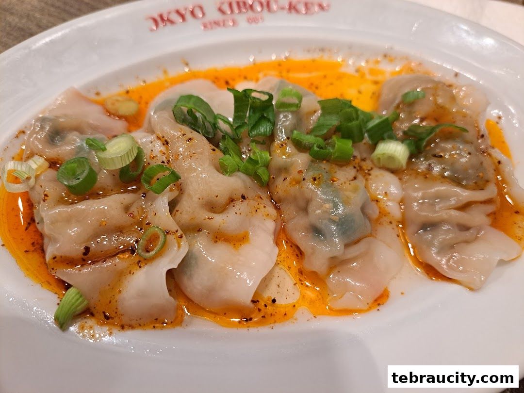 A plate of delicious dumplings in chili oil, garnished with chopped green onions.