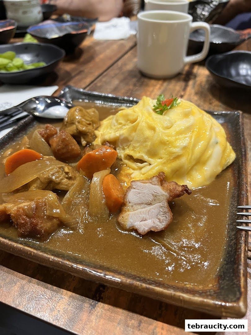 A close-up of a Japanese curry dish with omelet and chicken on a wooden table.